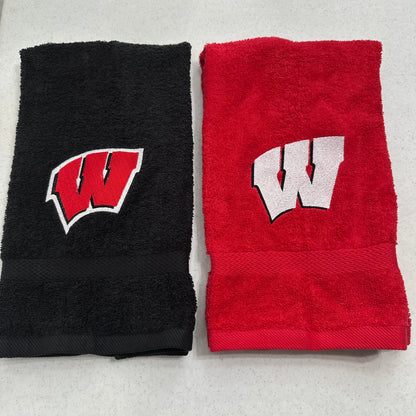 Two folded towels side by side on a light gray surface: one black towel with a red and white embroidered 'W' logo, and one red towel with a white and black embroidered 'W' logo.