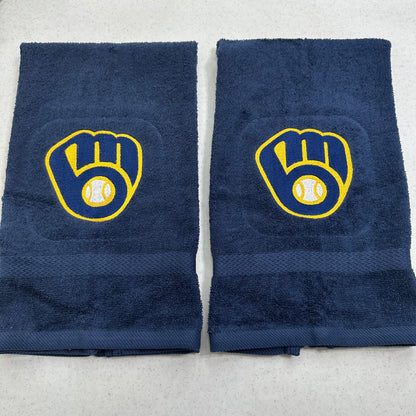 Two navy blue towels with yellow and white Milwaukee Brewers baseball glove and ball logo embroidered on the front, laid flat on a light gray surface.