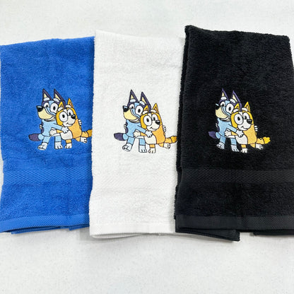 Three folded towels in blue, white, and black, each featuring cartoon bluey and bingo dog characters embroidered near the top center.