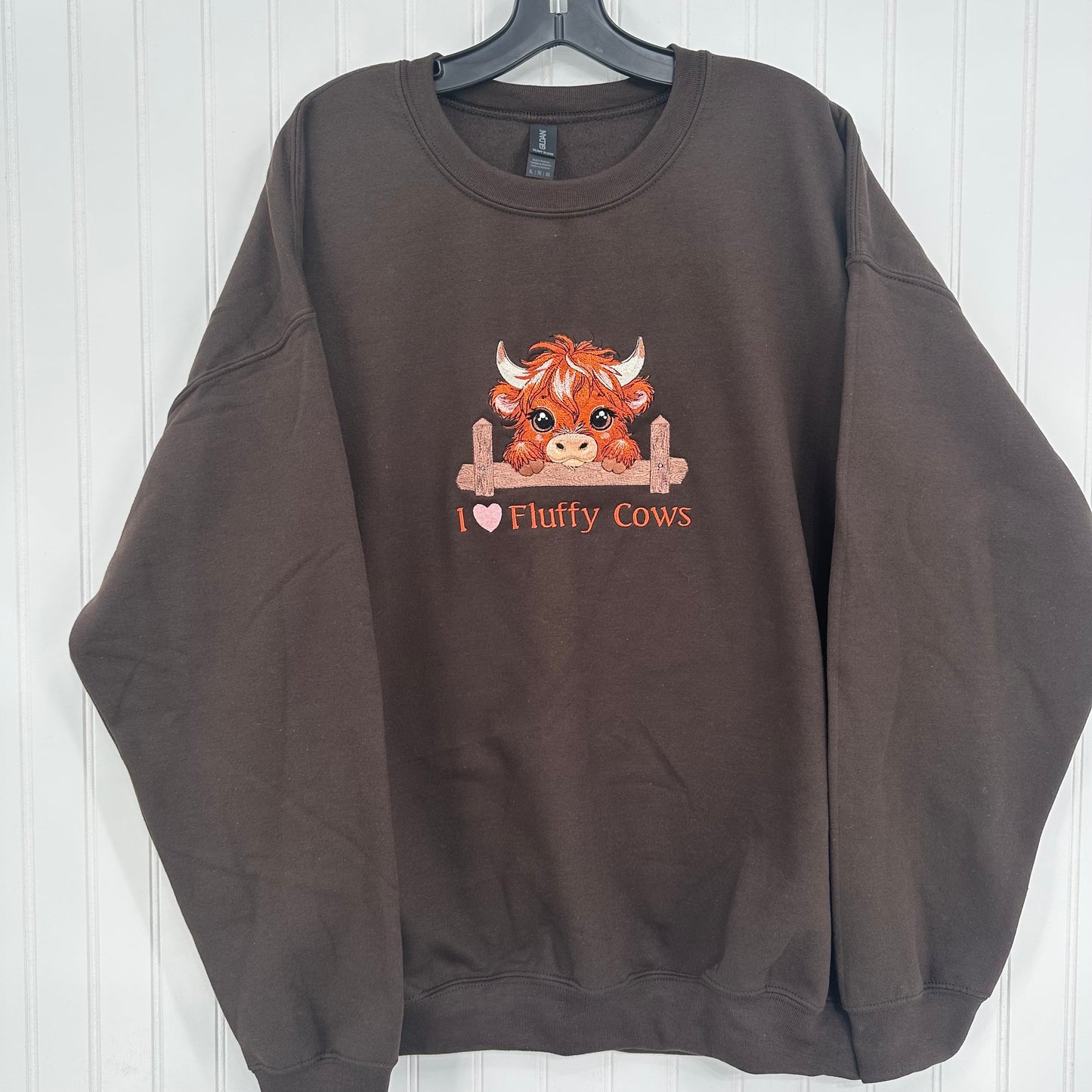 embroidered highland cow with a heart and text on a brown sweatshirt hanging up