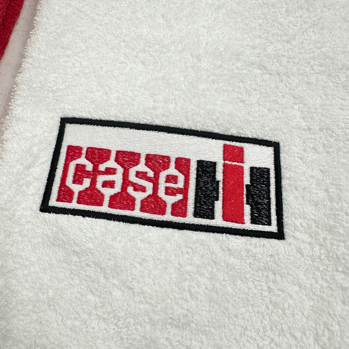 A close-up of a white textured fabric, likely a towel or blanket, featuring an embroidered rectangular logo with the word 'case' in red and 'li' in black and red, outlined in black.