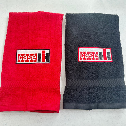 Two folded towels side by side on a light gray surface: a red towel on the left and a dark charcoal gray towel on the right, each with a rectangular embroidered Case IH logo patch on the front.