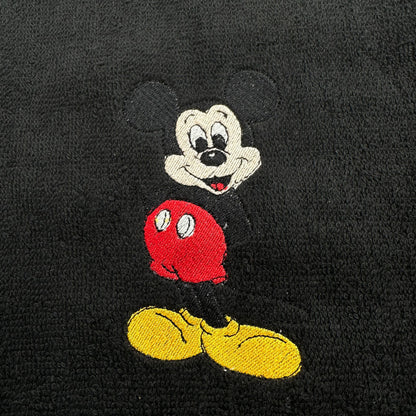 A close-up of a black textured fabric, likely a towel or blanket, featuring an embroidered Mickey Mouse character.