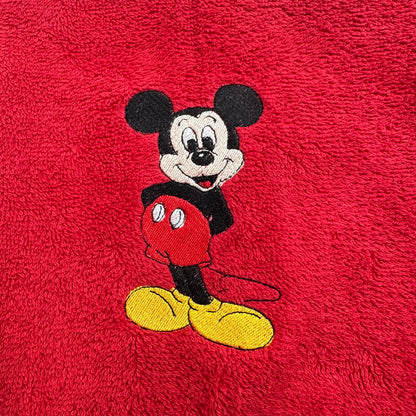 A close-up of a red textured fabric, likely a plush towel or blanket, featuring an embroidered Mickey Mouse character in the center.