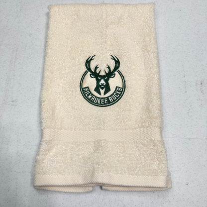 An off-white terry cloth hand towel featuring the Milwaukee Bucks logo embroidered in dark green in the center, laid flat on a light gray speckled surface.