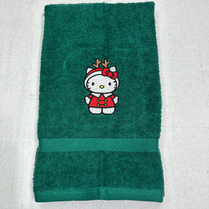 A dark green terry cloth towel featuring an embroidered Hello Kitty character in a red holiday outfit with reindeer antlers, laid flat on a light textured surface.