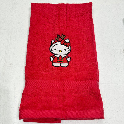 A folded red terry cloth towel featuring an embroidered Hello Kitty character wearing a holiday outfit with reindeer antlers, displayed on a light gray textured background.