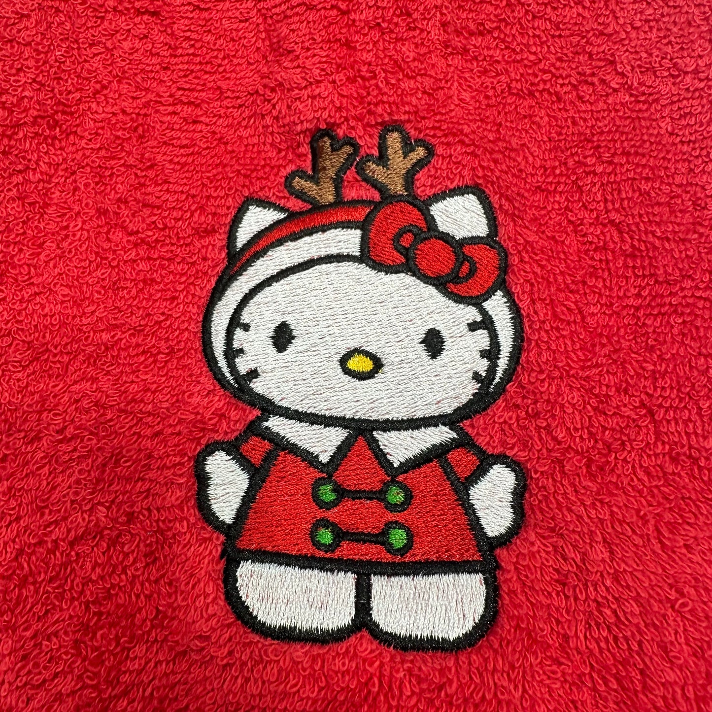 An embroidered Hello Kitty character patch wearing a red holiday outfit with reindeer antlers and a red bow, placed on a textured red fabric background.
