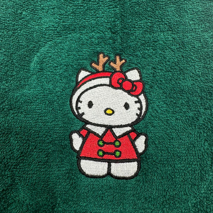 A close-up of a green textured fabric, likely a towel, featuring an embroidered Hello Kitty character wearing a red holiday sweater and reindeer antlers.