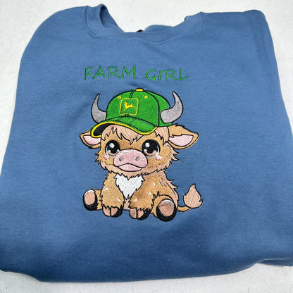 highland cow embroidered with a green hat on a blue sweatshirt