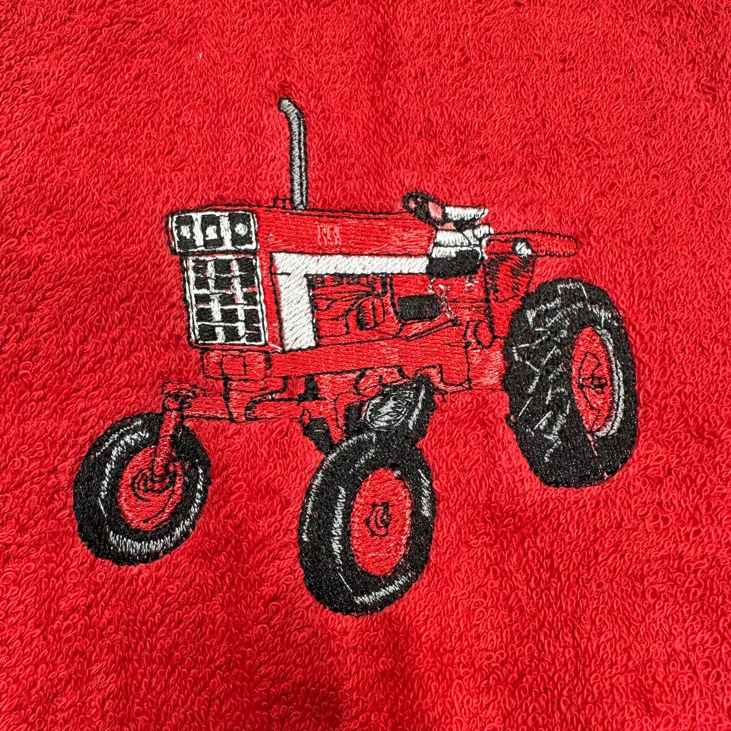 A close-up of a red textured fabric, likely a towel or blanket, featuring an embroidered design of a red and white tractor with black wheels.