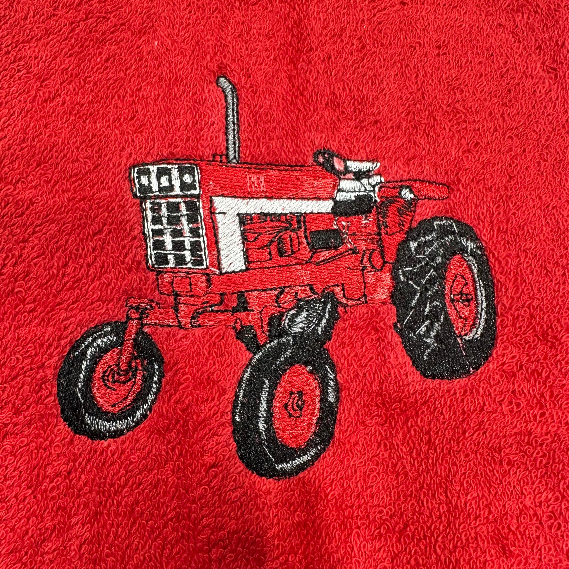 A close-up of a red textured fabric, likely a towel or blanket, featuring an embroidered design of a red and white tractor with black wheels.