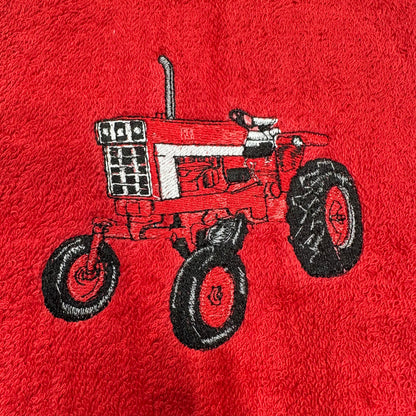 A close-up of a red textured fabric, likely a towel or blanket, featuring an embroidered design of a red and white tractor with black wheels.