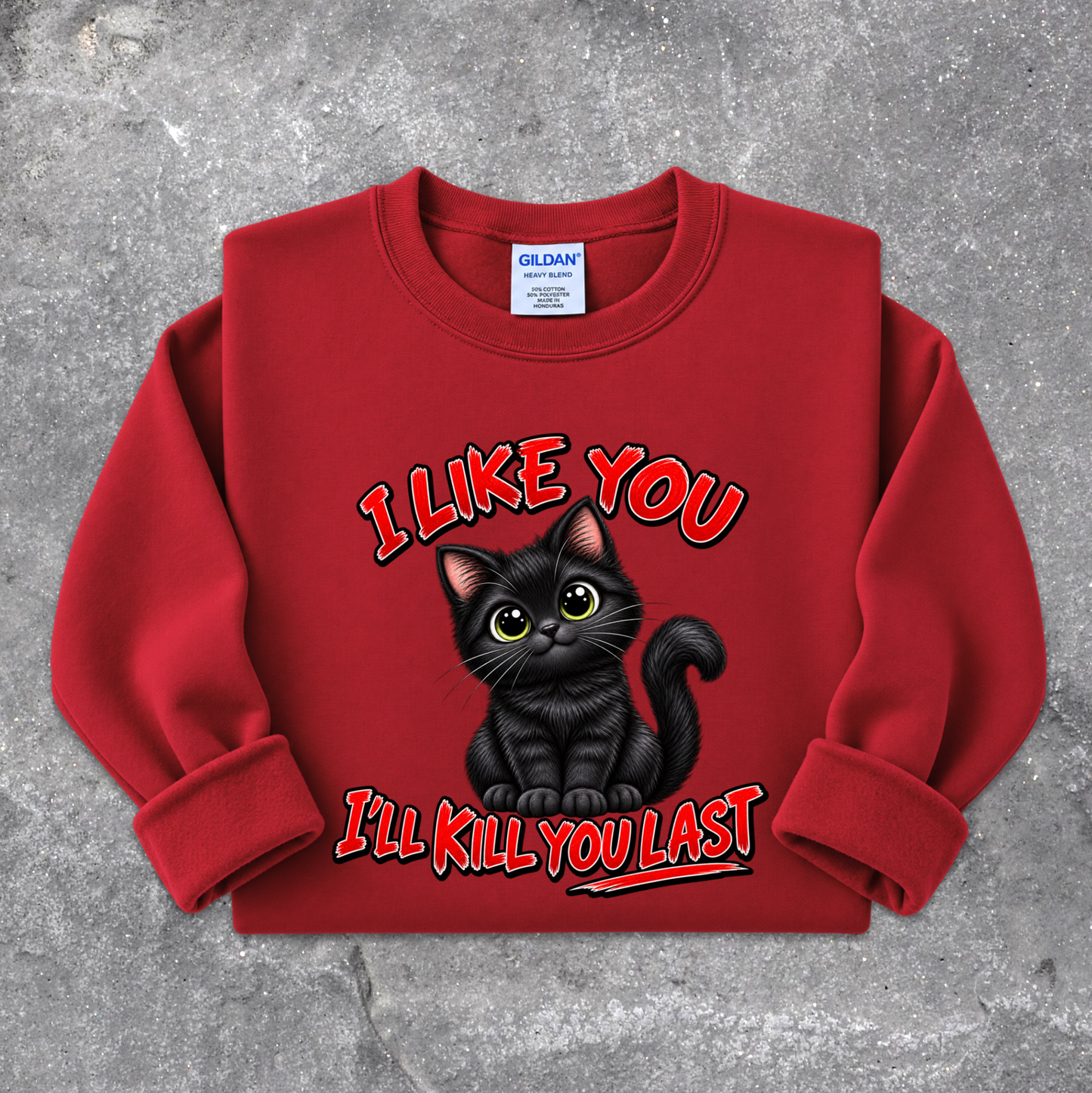 A red crewneck sweatshirt featuring a graphic of a black cat with the text 'I LIKE YOU I'LL KILL YOU LAST' in red and black, laid flat on a textured gray background. The neck label shows Gildan.