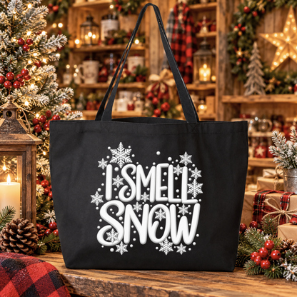A black canvas tote bag with the phrase 'I SMELL SNOW' in white lettering and white snowflakes, displayed on a rustic wooden table in a cozy, decorated Christmas setting.