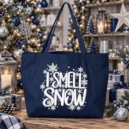 A navy blue canvas tote bag with white 'I SMELL SNOW' text and snowflake graphics, displayed on a rustic wooden table surrounded by Christmas decorations including a tree, lanterns, and wrapped gifts.