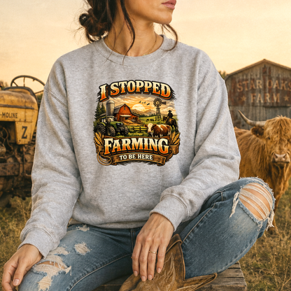 woman wearing gray sweatshirt with farm scene graphic that says I stopped farming to be here on it