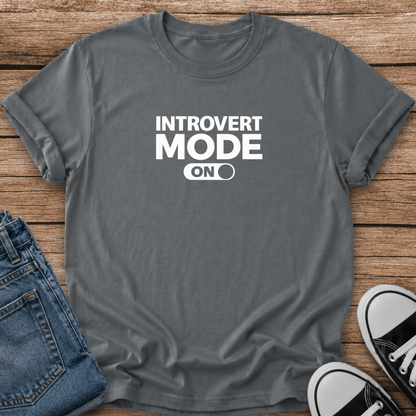 A dark gray graphic t-shirt with the text 'INTROVERT MODE ON' in white, styled in a flat lay on a wooden background with blue jeans and black-and-white sneakers.