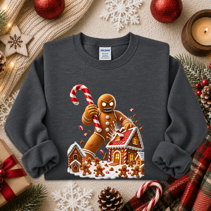 A dark gray crewneck sweatshirt featuring a festive Christmas gingerbread graphic, laid flat on a cozy holiday-themed background with a candle, pinecones, and red ornaments.