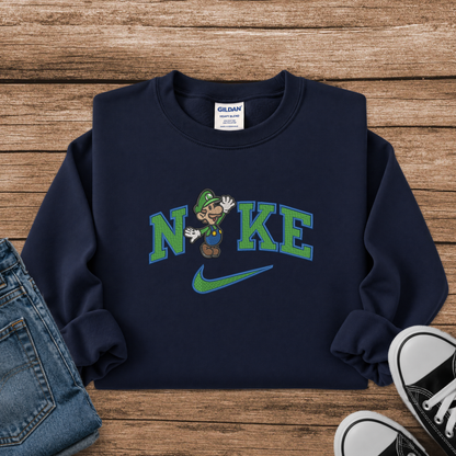 A navy blue crewneck sweatshirt featuring a graphic of Luigi with the word 'NIKE' and a Nike swoosh, styled in a flat lay on a wooden background with jeans and sneakers.