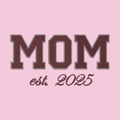 Embroidered-style text reading “MOM est. 2025” on a solid pink background.