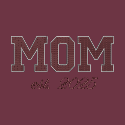 Embroidered collegiate-style 'MOM' lettering in maroon with a light gray outline, above the script text 'est. 2025' on a matching maroon background.