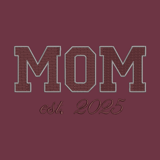 Embroidered collegiate-style 'MOM' lettering in maroon with a light gray outline, above the script text 'est. 2025' on a matching maroon background.