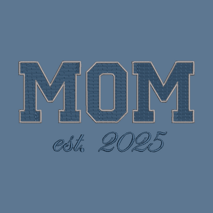 A blue graphic design featuring the word 'MOM' in large varsity-style block letters with a stitched denim-like texture and a tan outline, above the script text 'est. 2025' on a solid blue background.