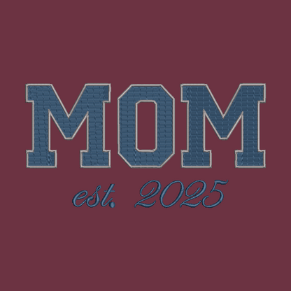 A graphic design featuring the word 'MOM' in large varsity-style block letters with a blue denim-like texture and a light outline, above the script text 'est. 2025' on a solid dark burgundy background.