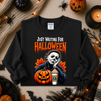 A black crewneck sweatshirt with a Halloween graphic of Michael Myers and a jack-o'-lantern, styled in a flat lay with pumpkins, a candle, and autumn leaves.