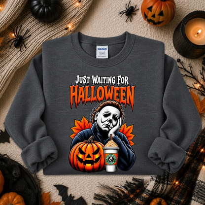 A dark gray sweatshirt with a Halloween graphic print featuring Michael Myers, a jack-o'-lantern, and a coffee cup, styled in a flat lay with autumn props.