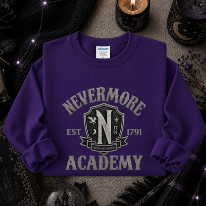 A purple long-sleeve sweatshirt with a 'Nevermore Academy' graphic printed on the front, styled in a cozy, dark themed flat-lay with candles, a knit scarf, and a plaid blanket.