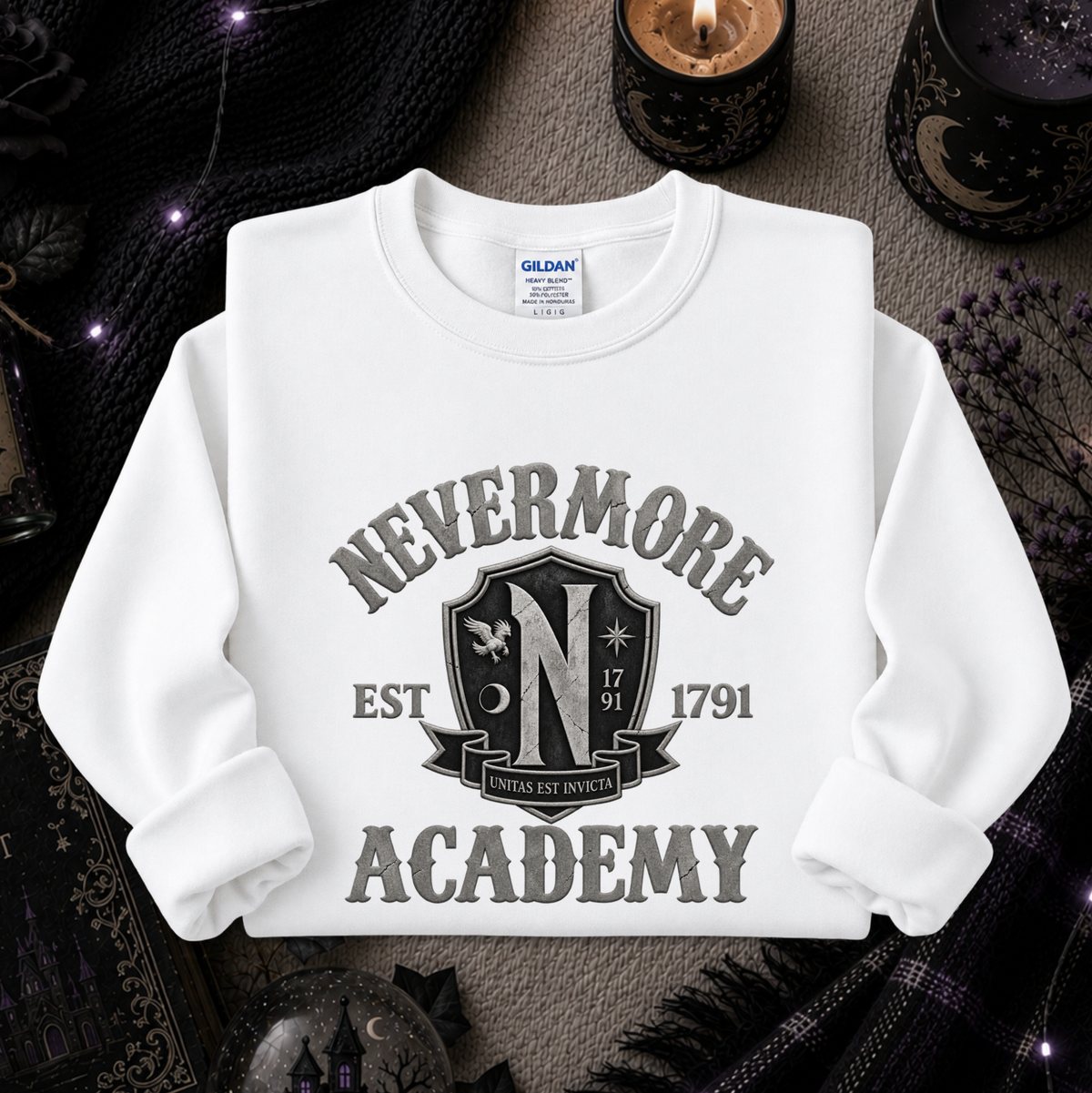 A white long-sleeve crewneck sweatshirt with a 'Nevermore Academy' graphic print, styled in a flat-lay on a dark, spooky background with candles, a black knit sweater, and occult-themed props.