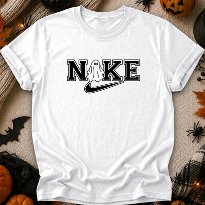 A white short-sleeve t-shirt with a black graphic print reading 'NIKE' where the 'I' is replaced by a ghost and a swoosh, styled in a flat-lay with Halloween decorations.