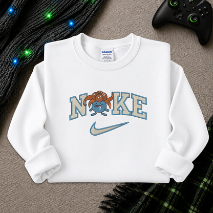 A white long-sleeve crewneck sweatshirt laid flat on a textured gray surface, featuring a custom graphic that reads 'NIKE' with a cartoon gloomy mascot and a light blue Nike swoosh. A Gildan brand tag is visible inside the collar.