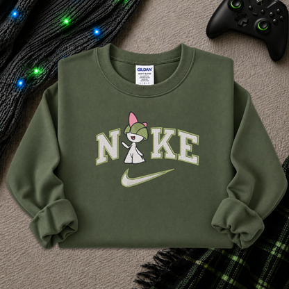 An olive green crewneck sweatshirt featuring a 'Nike' graphic with a cartoon character and a green swoosh, styled in a flat lay with a black knit sweater, a game controller, and a plaid blanket.