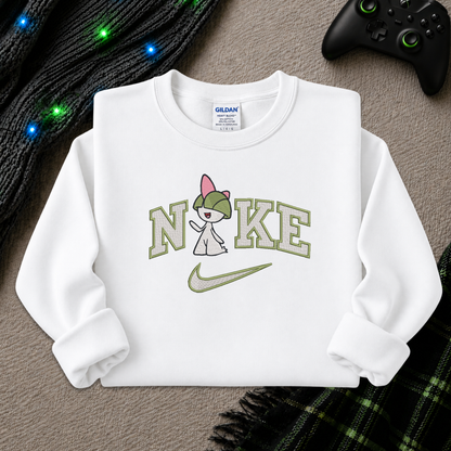 A white long-sleeve crewneck sweatshirt laid flat on a textured gray surface, featuring a graphic print of the word 'NIKE' styled with a pokemon Raltz cartoon character wearing a pink beanie and a green swoosh. The neck label shows Gildan branding.
