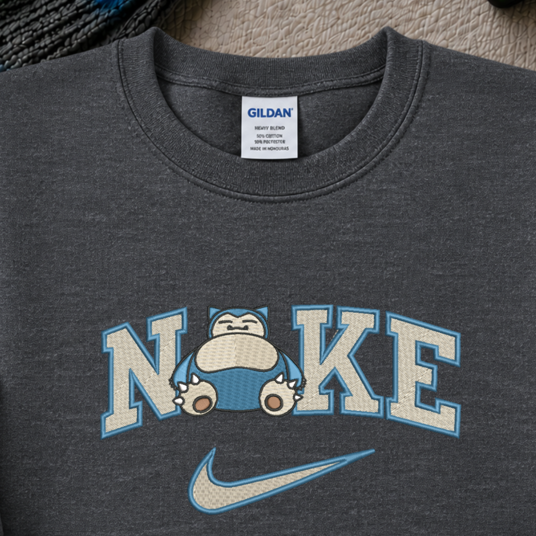 Close-up of a dark heather gray Gildan t-shirt featuring a custom 'Nike' style graphic with the word 'NOKE' and Snorlax, with a light blue Nike swoosh underneath.