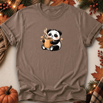 A taupe brown short-sleeve t-shirt with a cute cartoon panda holding a mug, laid flat on a neutral background with autumn-themed props like a pumpkin, pine branches, and leaves.