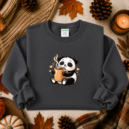 A dark charcoal gray crewneck sweatshirt featuring a cute cartoon panda holding a mug, styled in a cozy autumn flat-lay with pinecones, a knit blanket, and a lit candle. The brand Gildan is visible on the inner neck label.