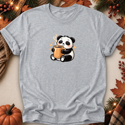 A light heather gray short-sleeve t-shirt featuring a cute cartoon panda holding an orange mug, styled in a flat-lay with autumn decorations like a pumpkin, pine branches, and leaves.