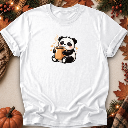 A white short-sleeve crewneck t-shirt featuring a cute cartoon panda holding an orange mug, styled in a flat-lay with autumn props like a pumpkin, pine branches, and leaves.
