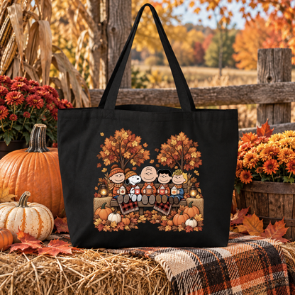 black canvas tote bag with a graphic design of the peanuts gang sitting on a bench cozy weather with pumpkins and autumn leaves
