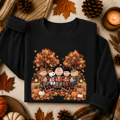 A black crewneck sweatshirt featuring a colorful graphic of the Peanuts characters Snoopy and Charlie Brown playing keyboards in an autumn park, surrounded by fall leaves, pinecones, and a candle.