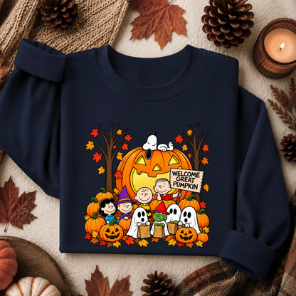 A navy blue sweatshirt featuring a colorful 'Welcome Great Pumpkin' Peanuts Halloween graphic, styled in a flat lay with autumn leaves, pinecones, and a lit candle.