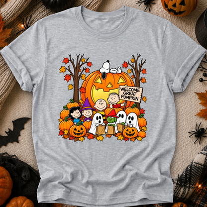 A heather gray short-sleeve T-shirt laid flat with a large colorful Halloween graphic on the front. The print shows Snoopy and Charlie Brown with pumpkins, ghosts, autumn trees, and a sign reading “Welcome Great Pumpkin.