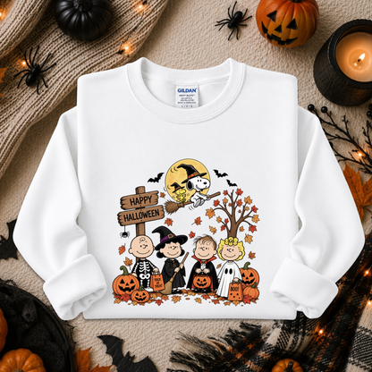 A white Gildan sweatshirt with a colorful 'Happy Halloween' cartoon graphic, styled in a flat-lay with seasonal props like pumpkins, a spider, and a candle.