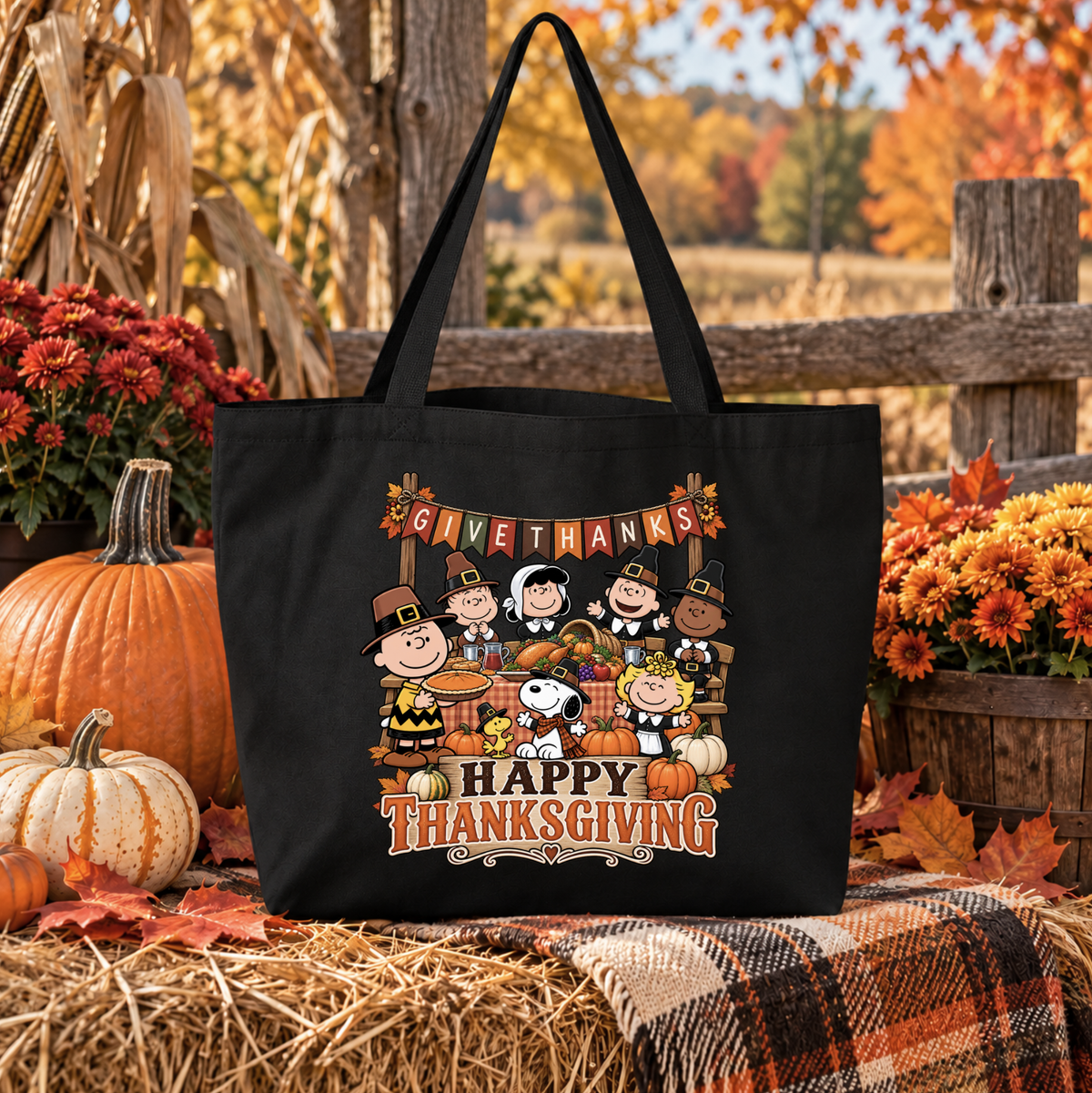 black canvas tote bag with a graphic of the peanuts gang sitting at a table eating thanksgiving dinner wearing pilgrim costumes and it says happy thanksgiving and give thanks