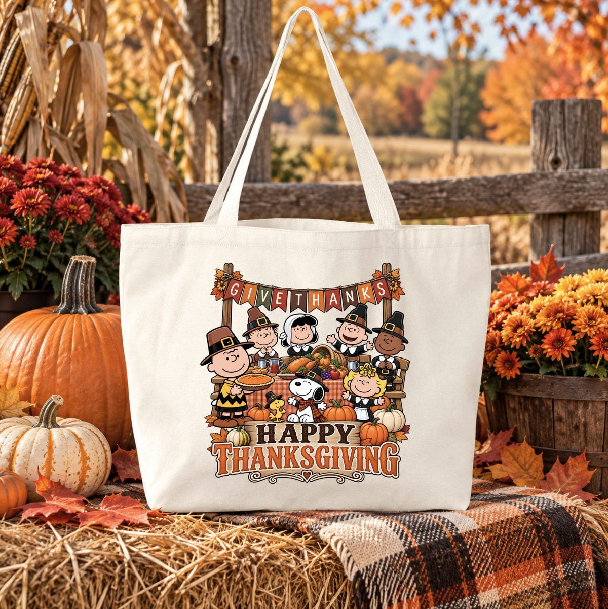 beige canvas tote bag with a graphic of the peanuts gang sitting at a table eating thanksgiving dinner wearing pilgrim costumes and it says happy thanksgiving and give thanks