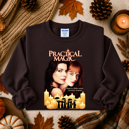 A dark brown crewneck sweatshirt featuring a 'Practical Magic' movie graphic print, styled in an autumn flat-lay setting with pinecones, leaves, and a candle.